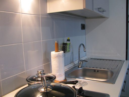Cucina moderna con lavandino, pentole e asciugamani da cucina su un piano bianco.