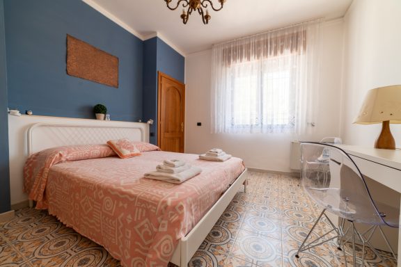 Camera da letto luminosa con un letto matrimoniale, decorazioni rosa e arredo semplice.