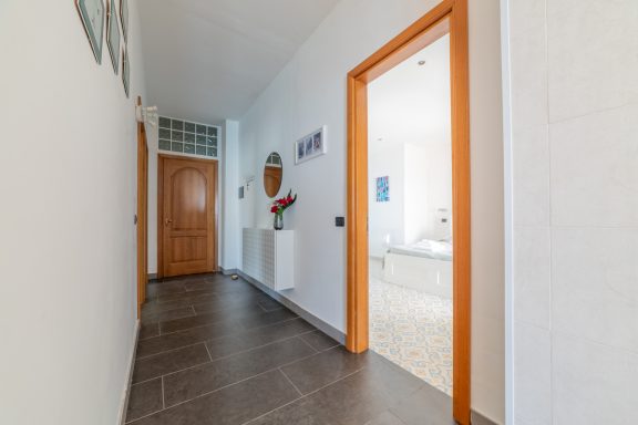 Corridoio luminoso con pareti bianche, porta in legno e pavimento in piastrelle scure.