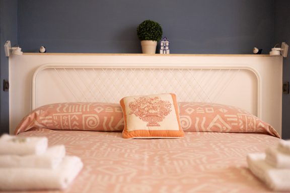Letto con biancheria arancione e decorazioni, piante e bottiglie sullo sfondo.