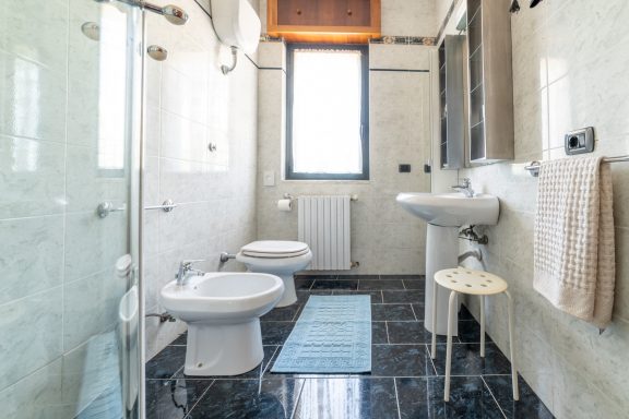 Bagno luminoso con doccia, bidet, lavabo e pavimento in marmo scuro.